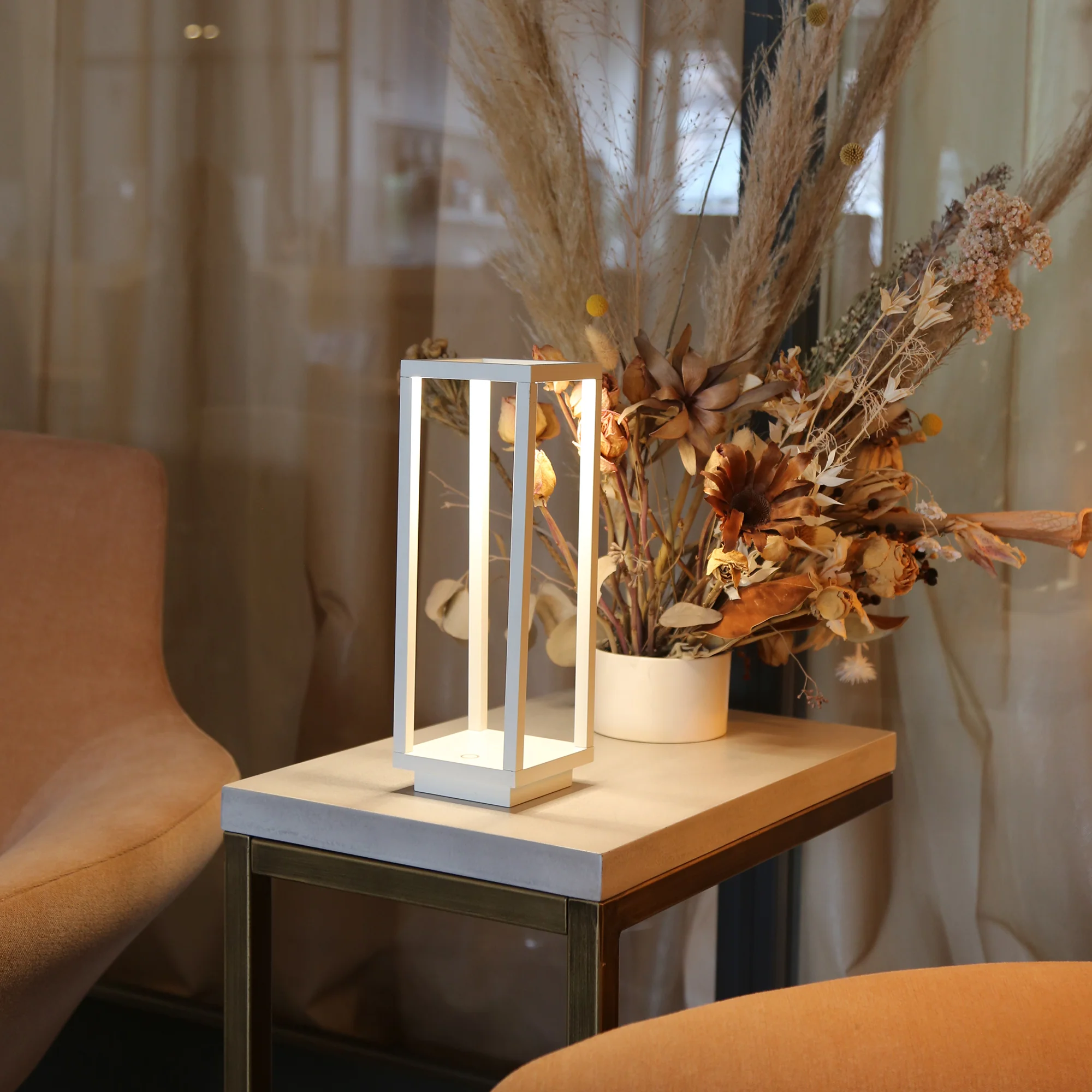 The white Home Cordless Lamp from Zafferano in a greeting room between two chairs on a table.