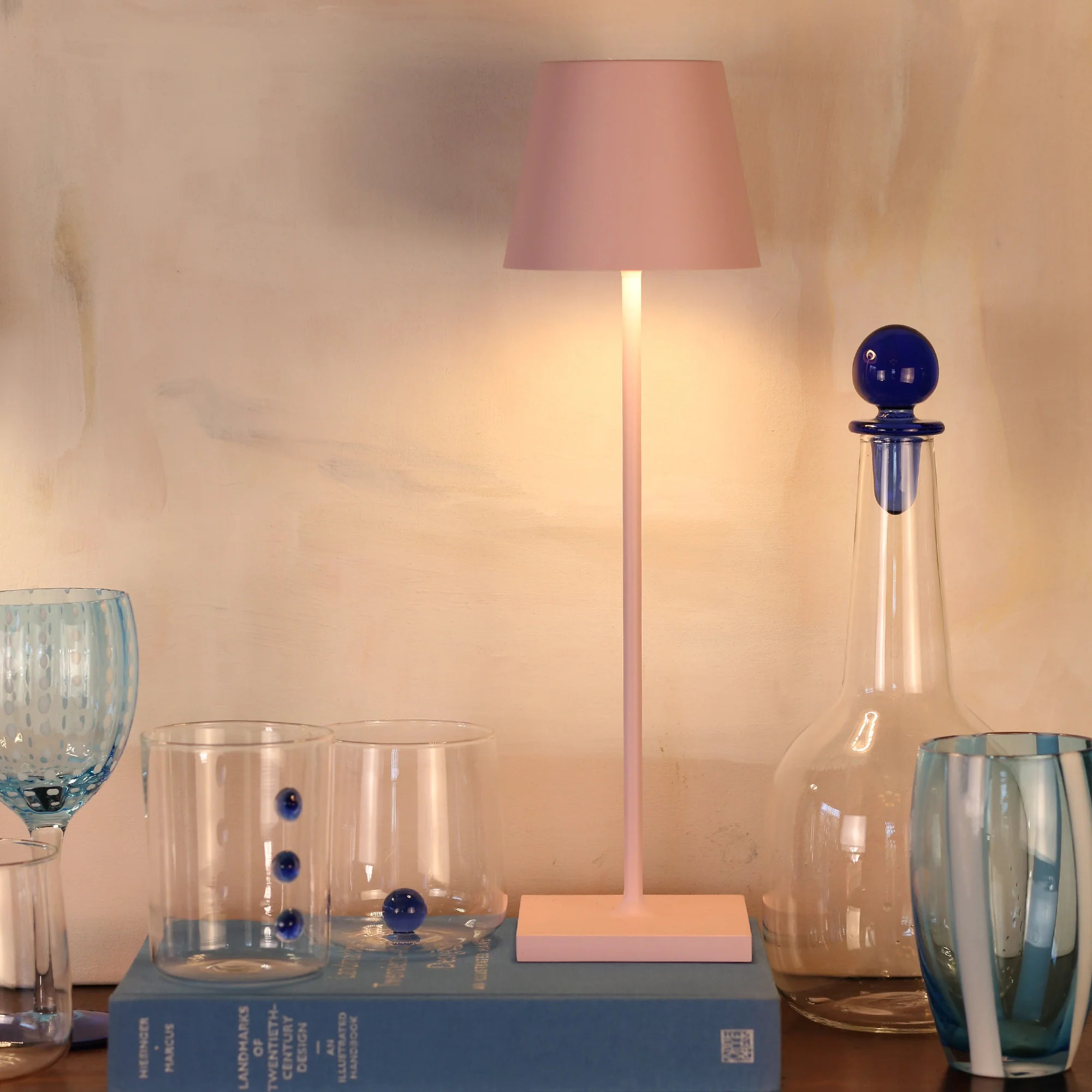 The pink Poldina Pro from Zafferano in a living room on top of a book and beside several glasses.