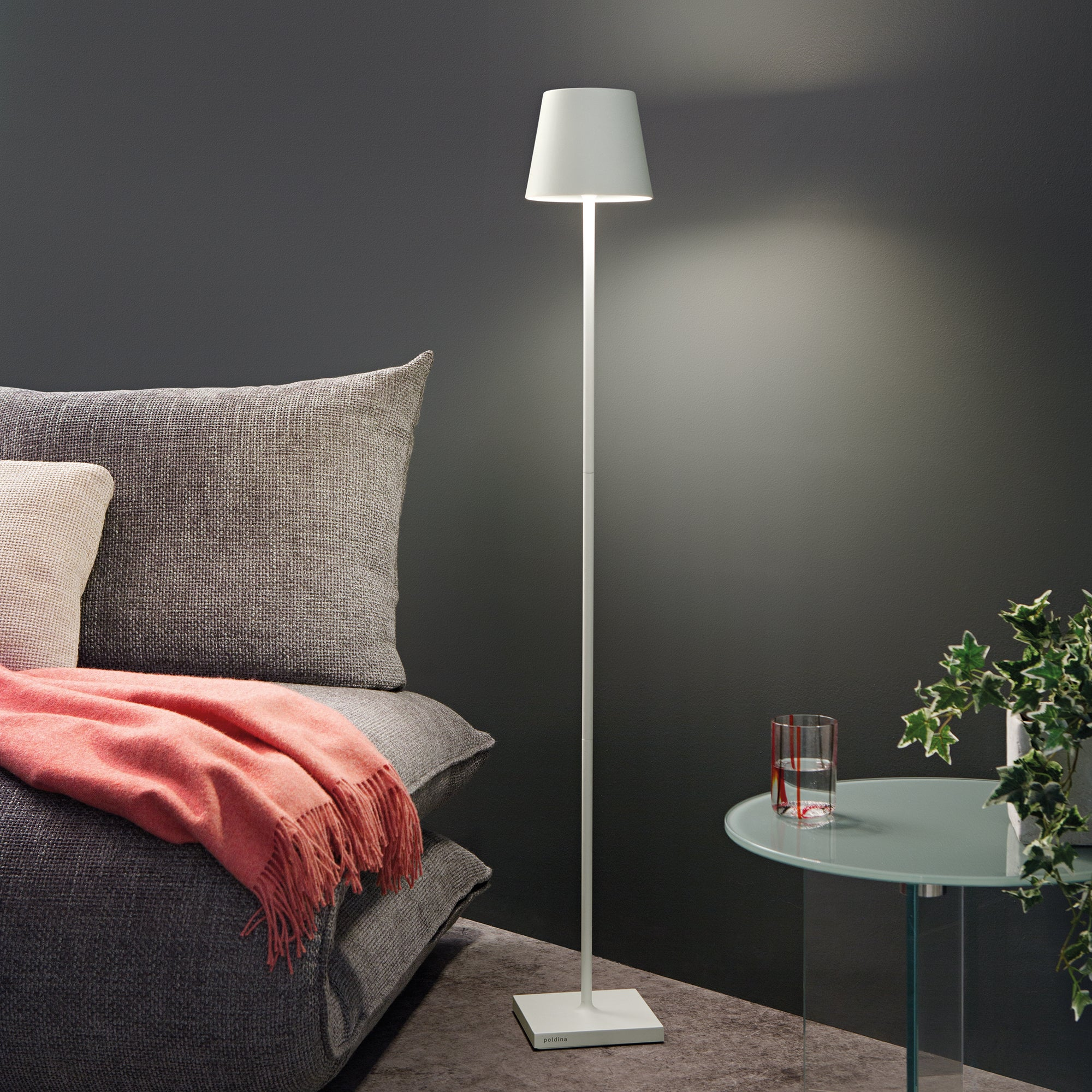 The white Poldina Pro L Floor Lamp from Zafferano in a guest bedroom beside a table and a bed.