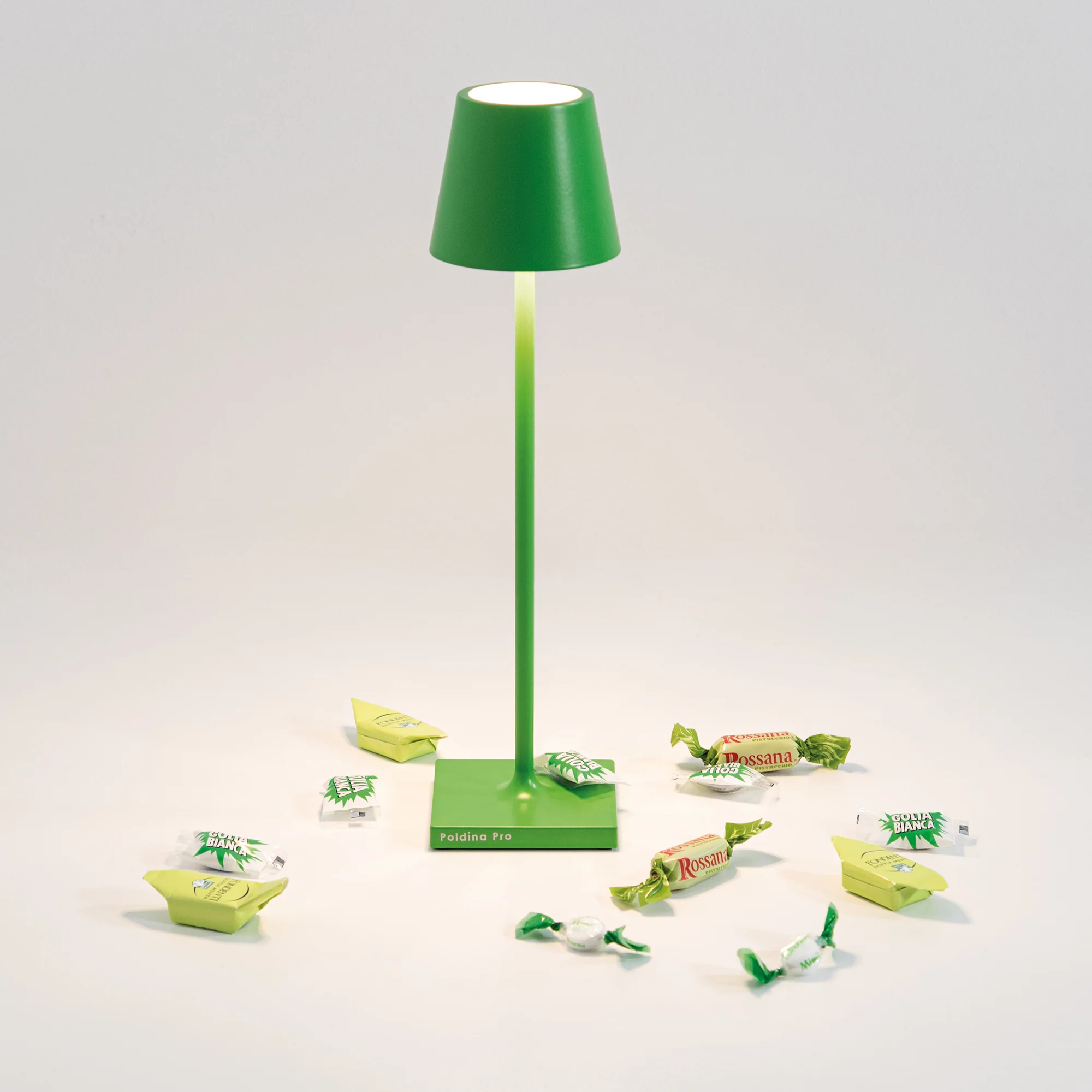 The apple green Poldina Pro Micro Cordless Lamp from Zafferano in a studio with various candies.