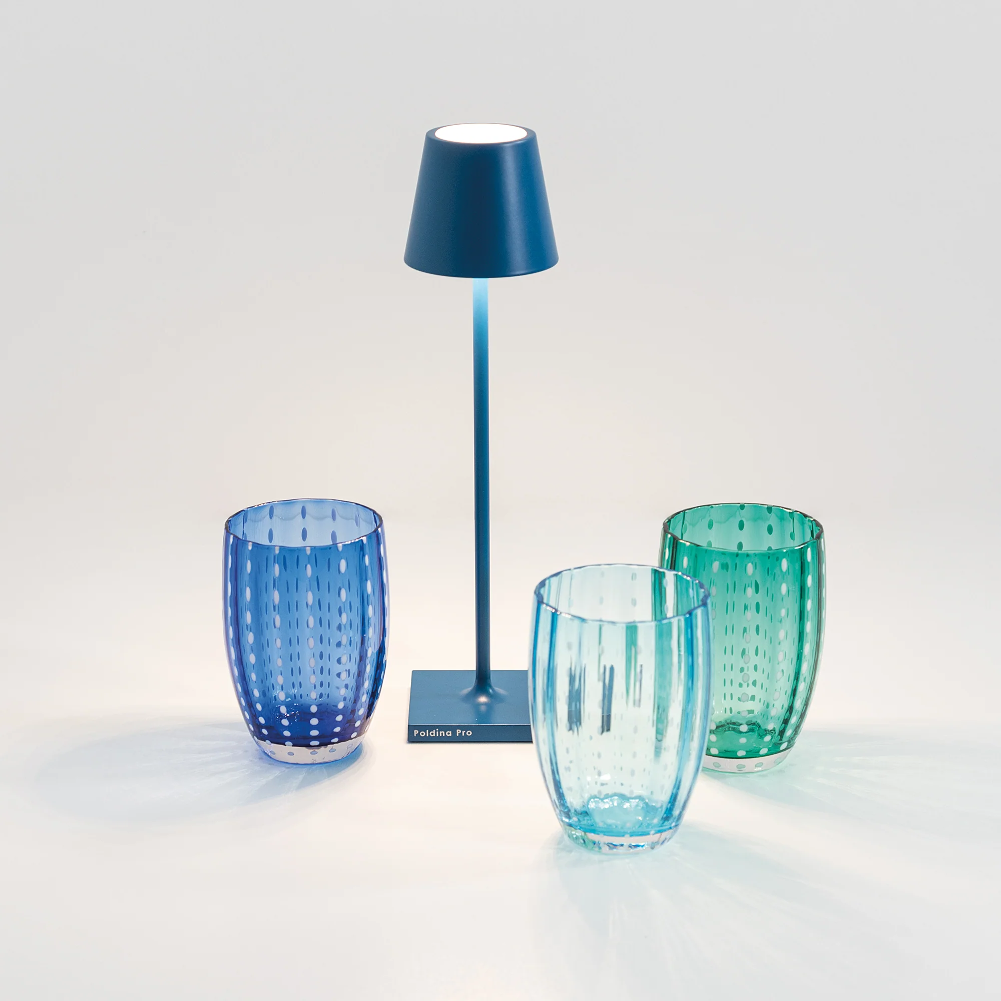 The capri blue Poldina Pro Micro Cordless Lamp from Zafferano beside a few drinking glasses.