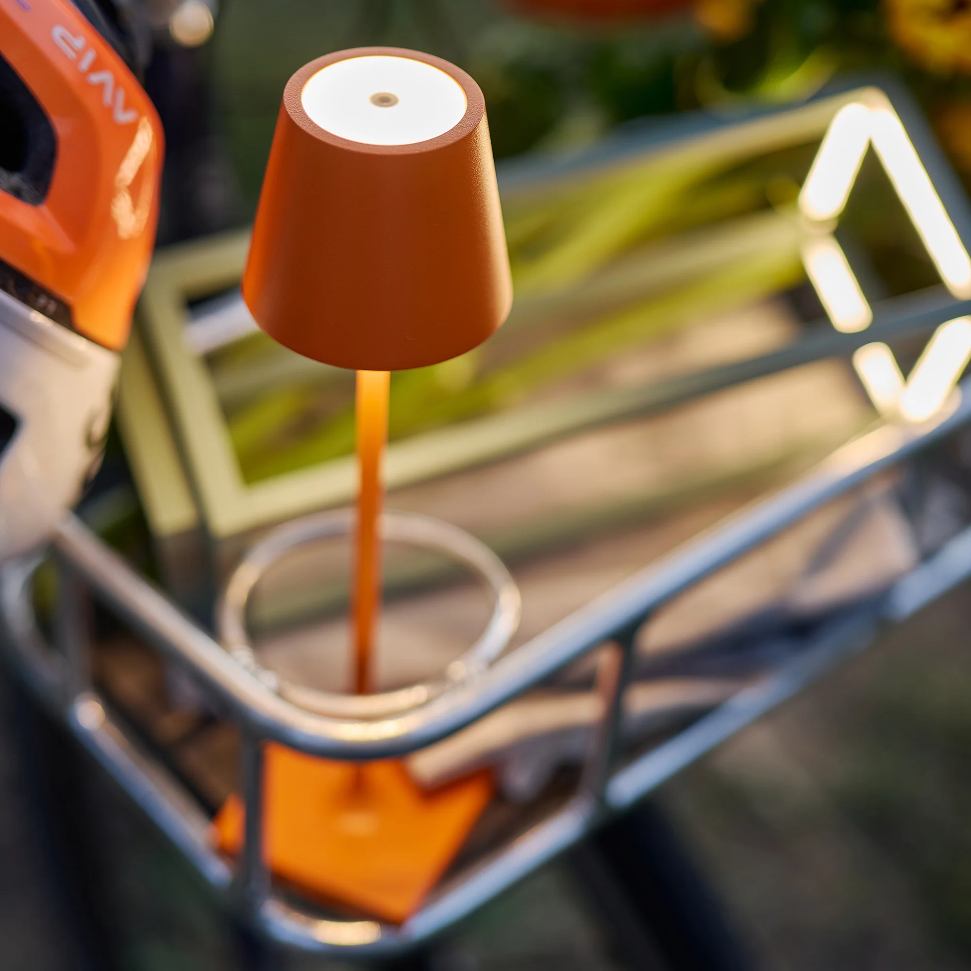 The orange Poldina Pro Micro Cordless Lamp from Zafferano in a garden.
