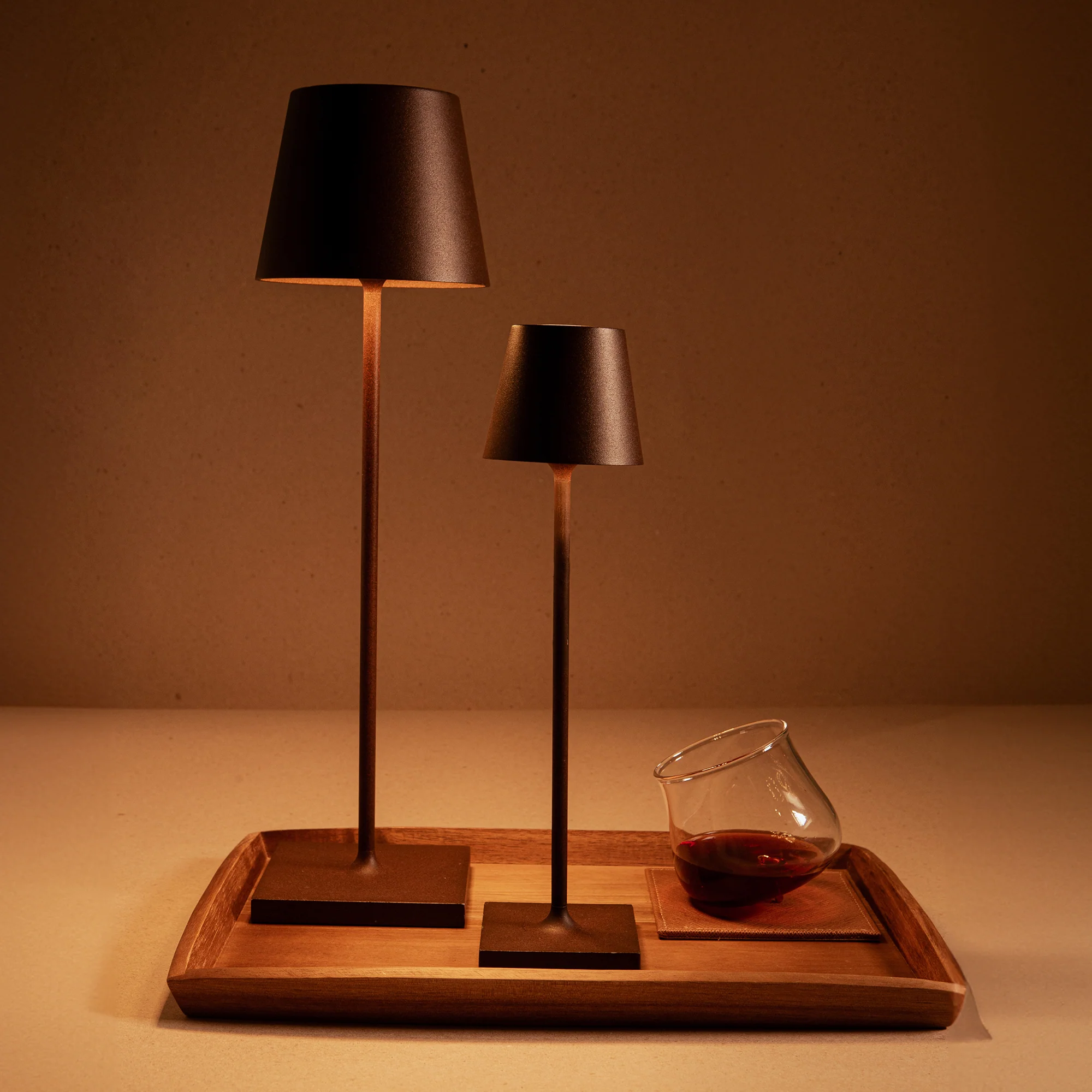 The rust Poldina Pro Micro Cordless Lamp from Zafferano on a bar tray with the Poldina Pro and a drink.