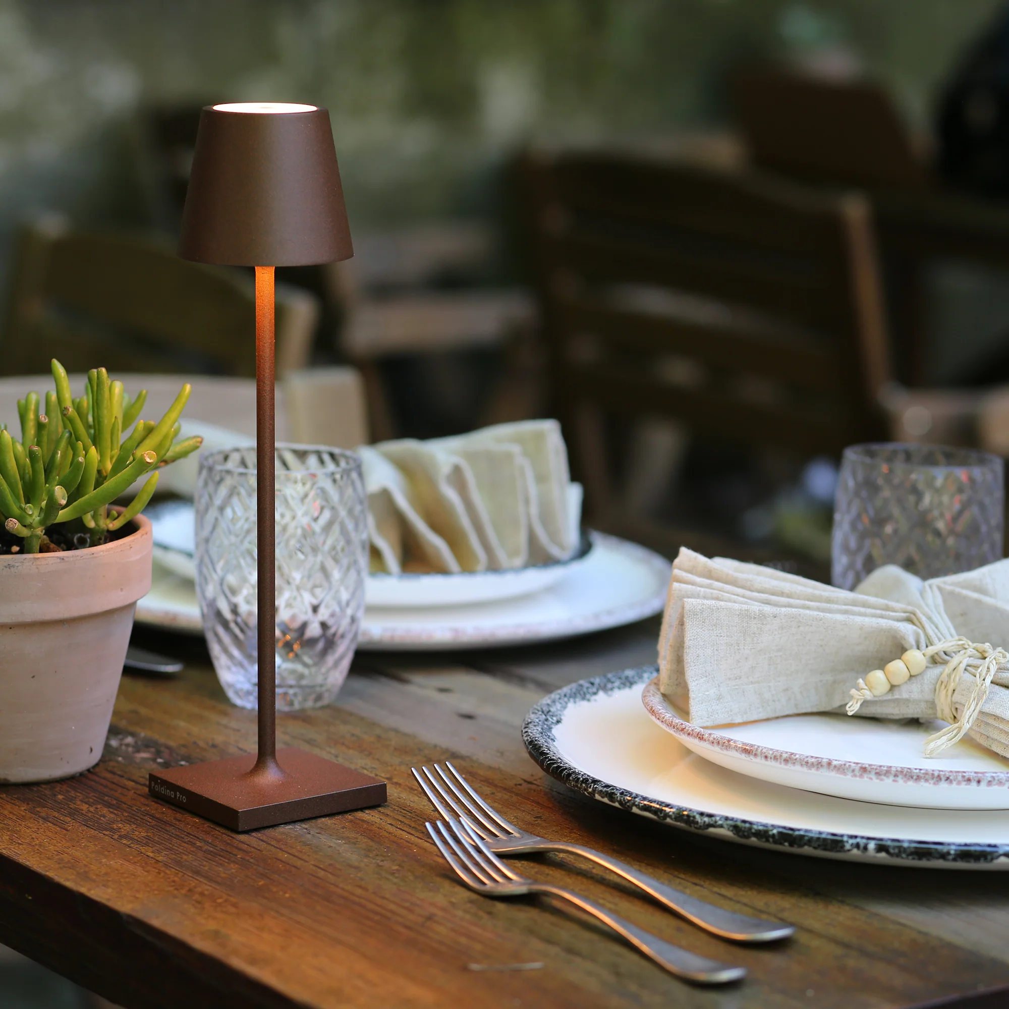 The rust Poldina Pro Micro Cordless Lamp from Zafferano on top of a table in an outdoor restaurant.