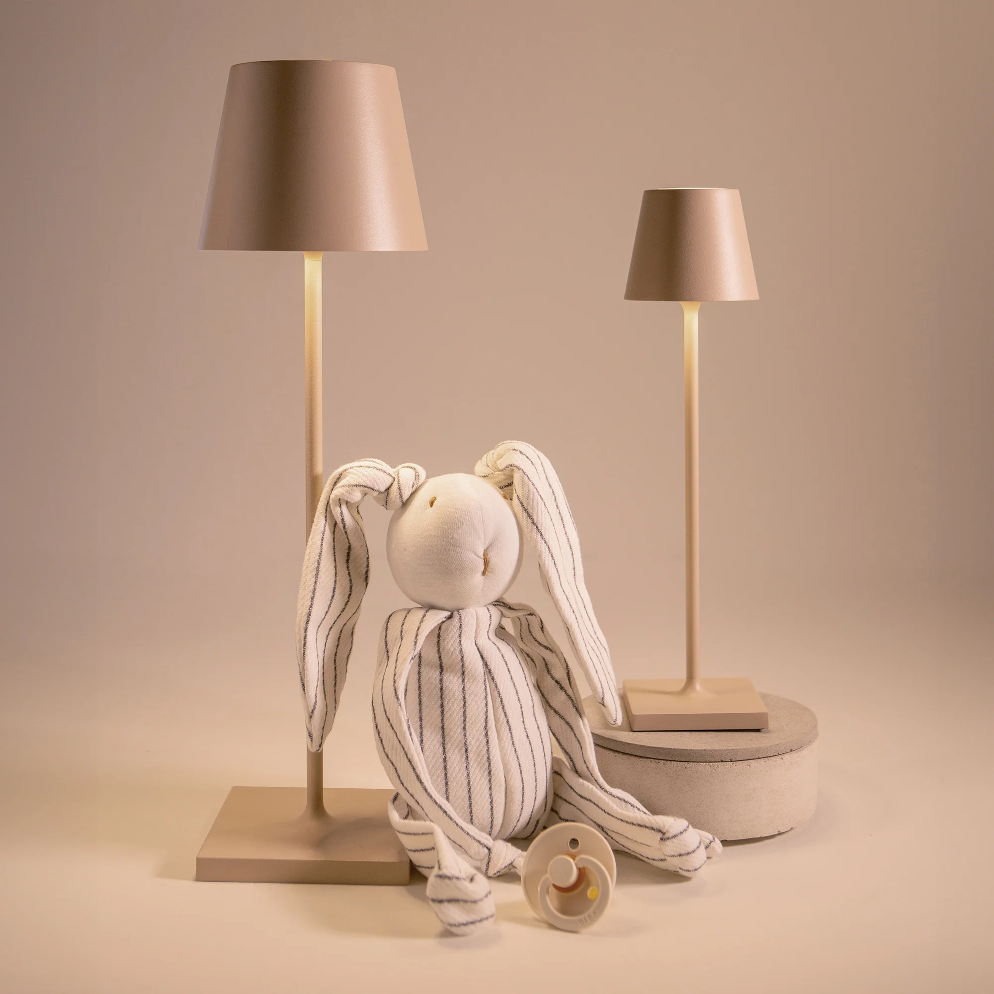 The sand Poldina Pro Micro Cordless Lamp from Zafferano in a studio next to a baby toy used as decor.