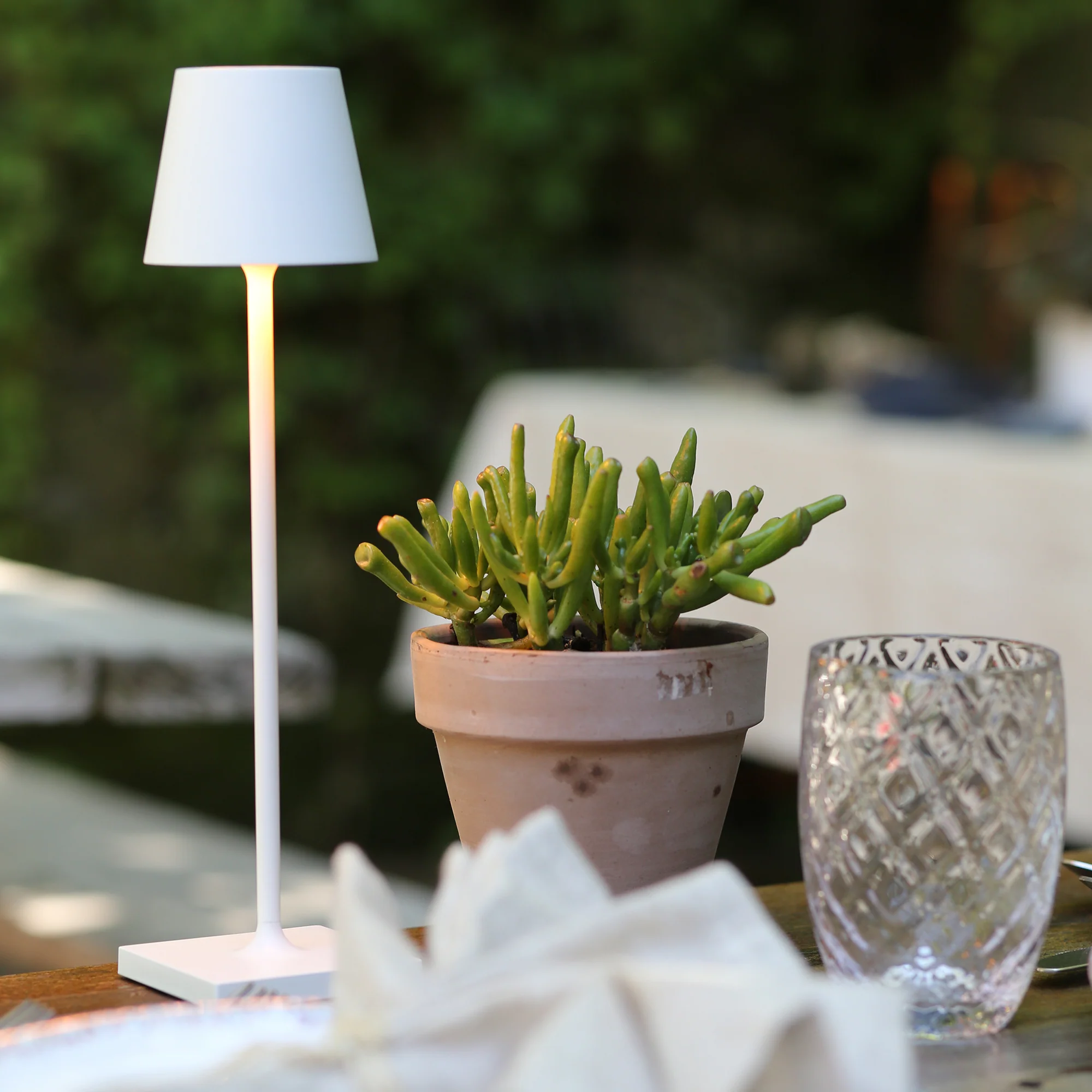 The white Poldina Pro Micro Cordless Lamp from Zafferano used on a table at an outdoor cafe.