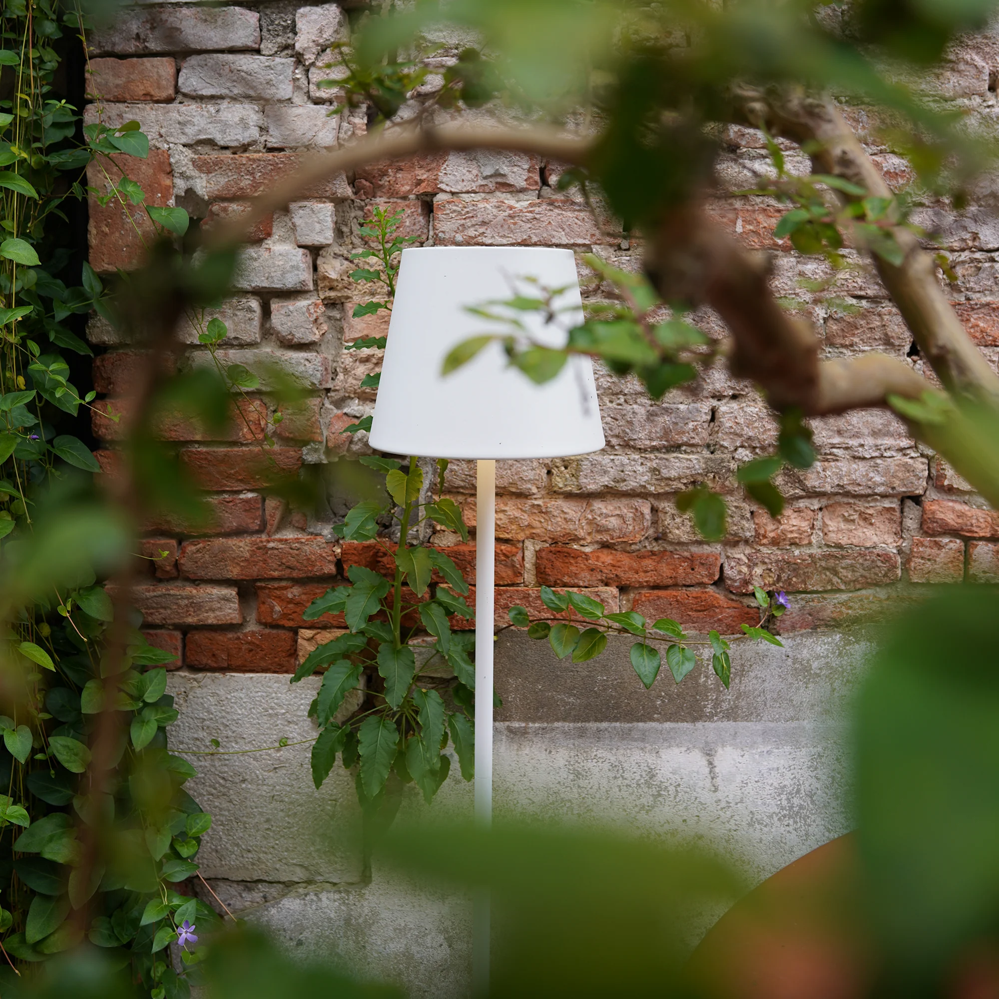 The white Poldina Pro XXL Floor Lamp from Zafferano in a garden.
