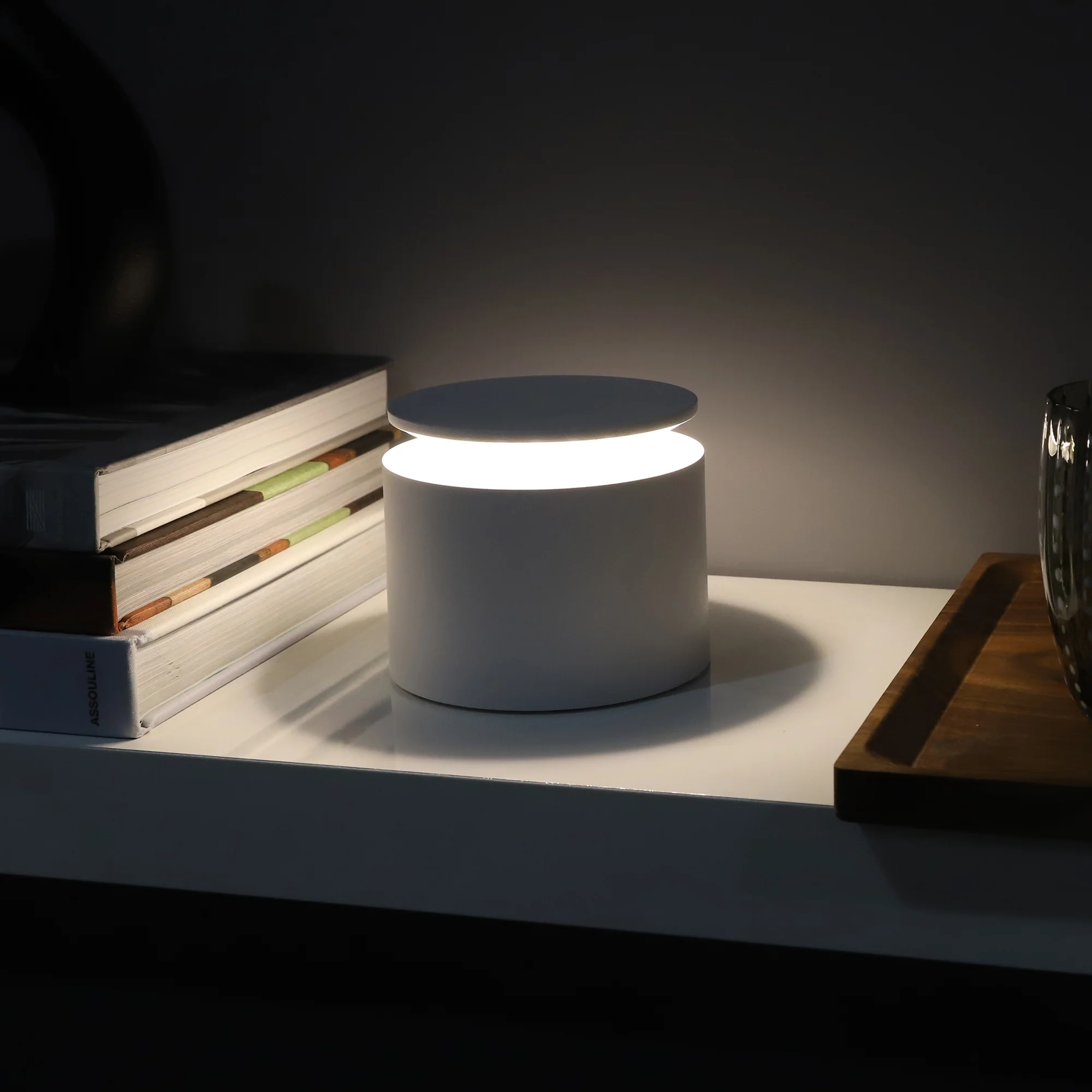 The white PushUp Pro Cordless Lamp from Zafferano on top of a bedside table with books, a tray and a glass.