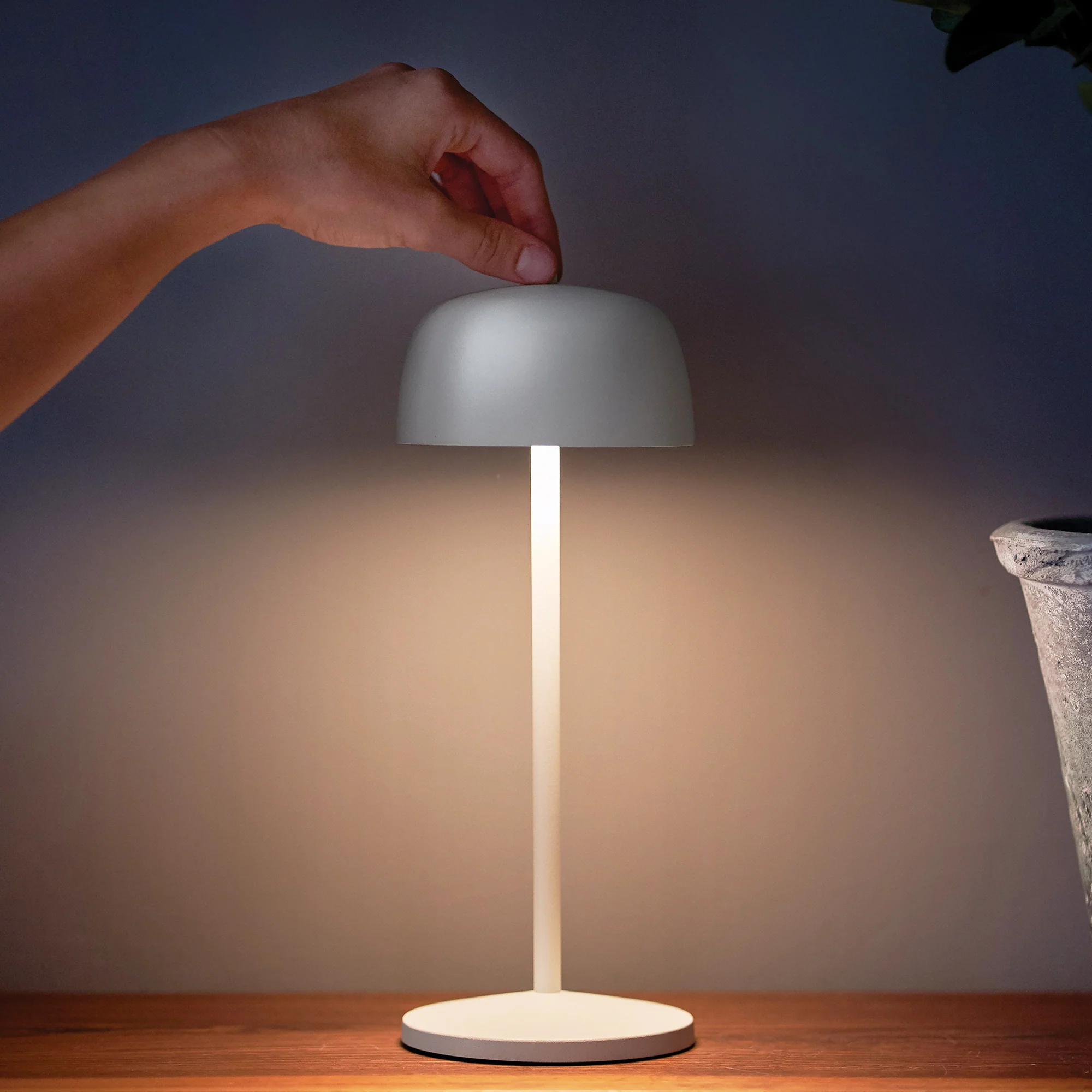 The matte white Theta Pro Cordless Lamp from Zafferano in a living space on a wooden surface.