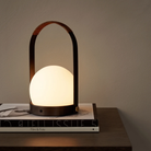 The bronzed brass Carrie Portable Table Lamp from Audo Copenhagen in a family area on top of a table with books.