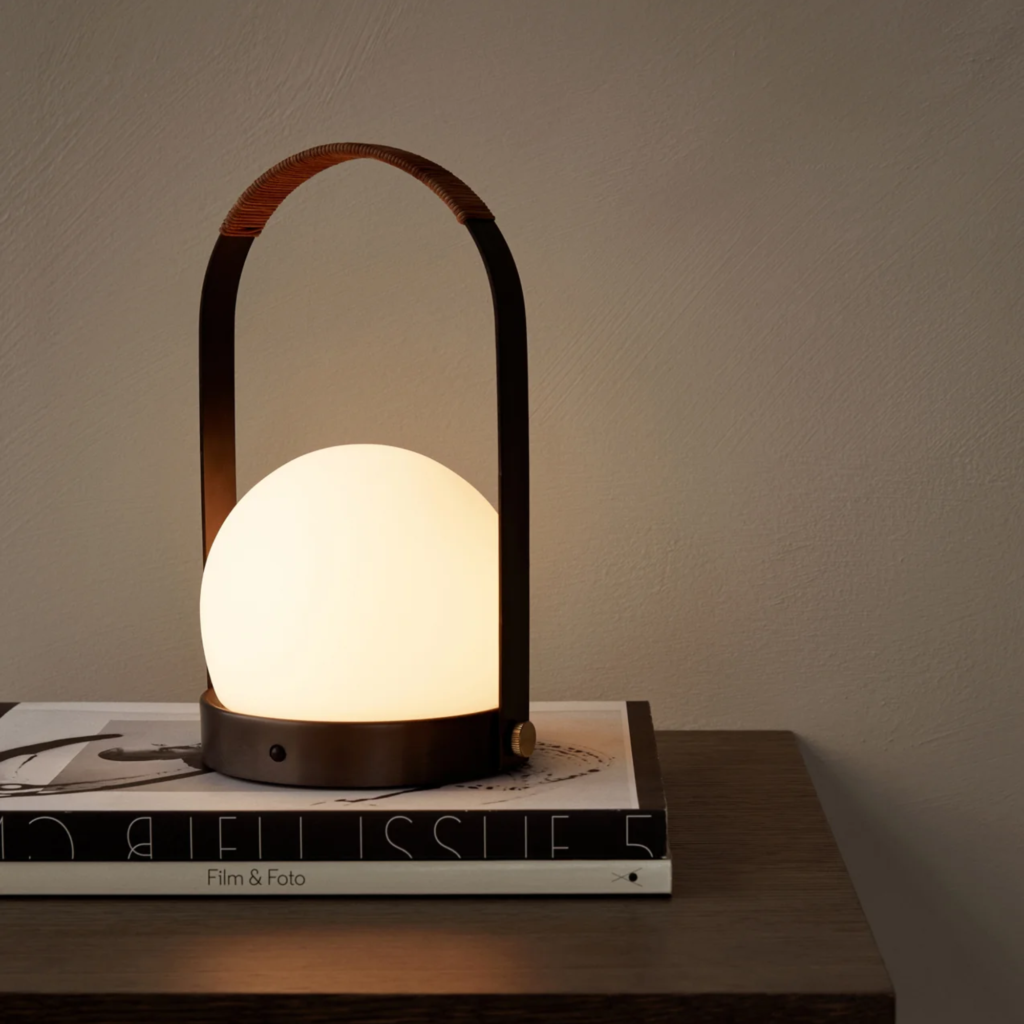 The bronzed brass Carrie Portable Table Lamp from Audo Copenhagen in a family area on top of a table with books.
