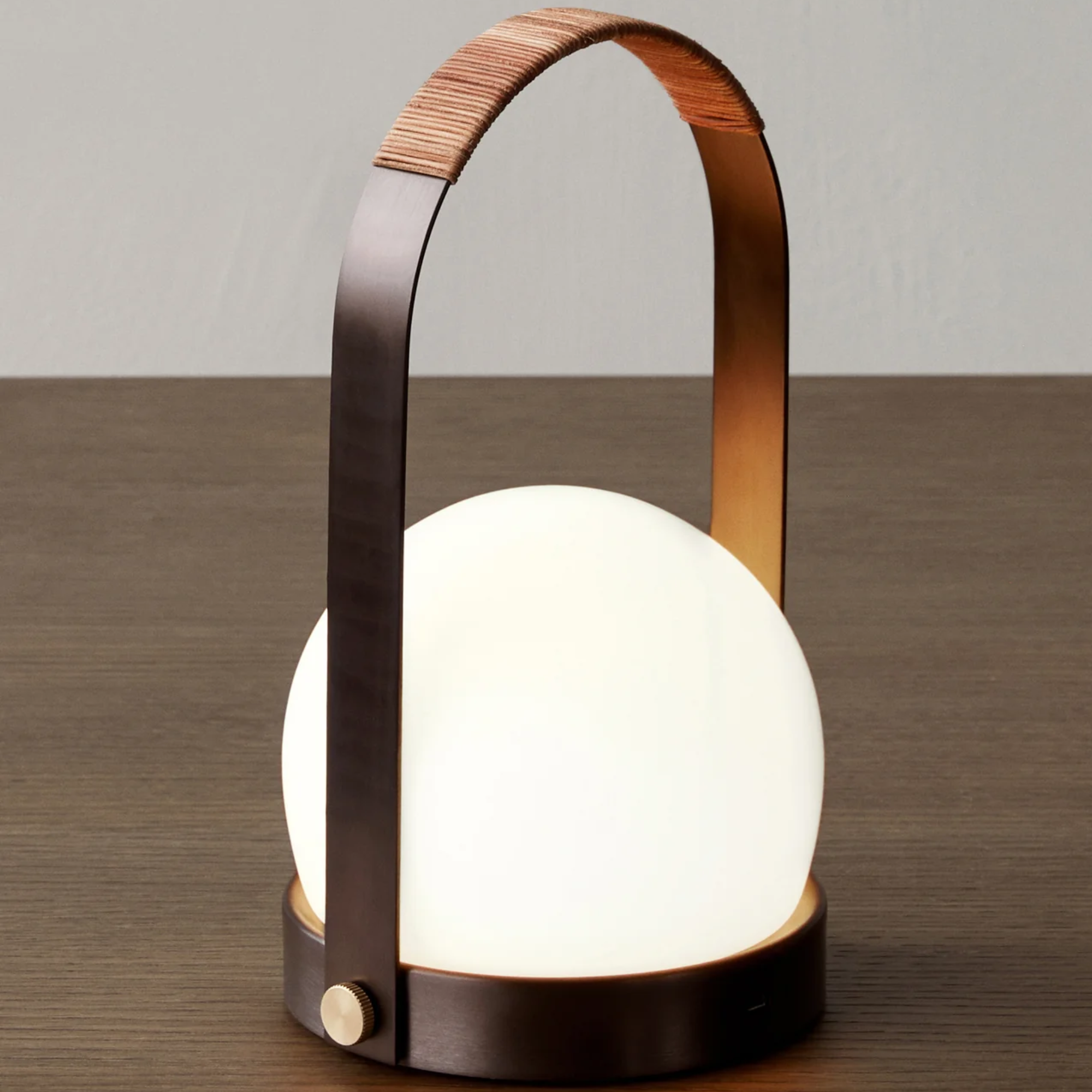The bronzed brass Carrie Portable Table Lamp from Audo Copenhagen on top of a table in a living space.