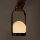 The bronzed brass Carrie Portable Table Lamp from Audo Copenhagen handheld in a studio.