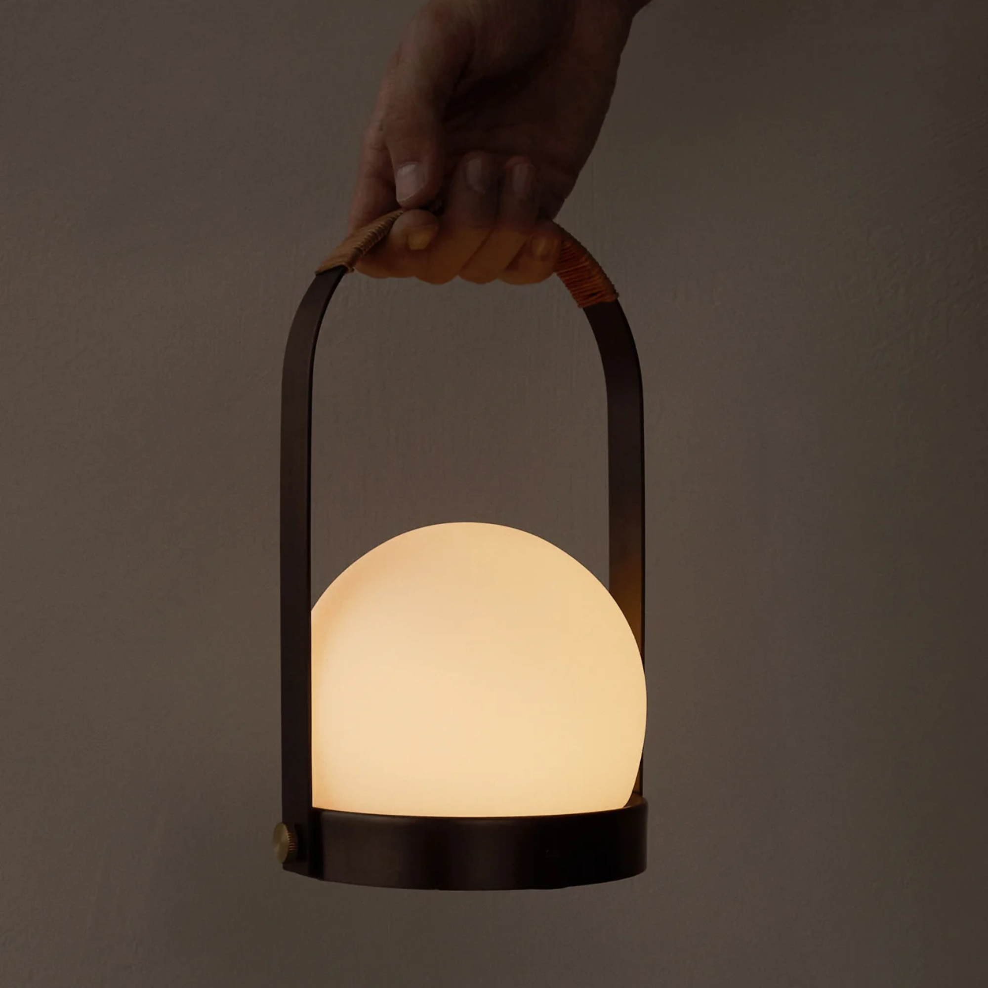 The bronzed brass Carrie Portable Table Lamp from Audo Copenhagen handheld in a studio.