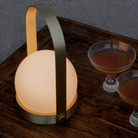 The brushed brass Carrie Portable Table Lamp from Audo Copenhagen on a dining table with drinks.