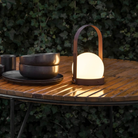 The burned red Carrie Portable Table Lamp from Audo Copenhagen on a table in an outdoor dining setting.