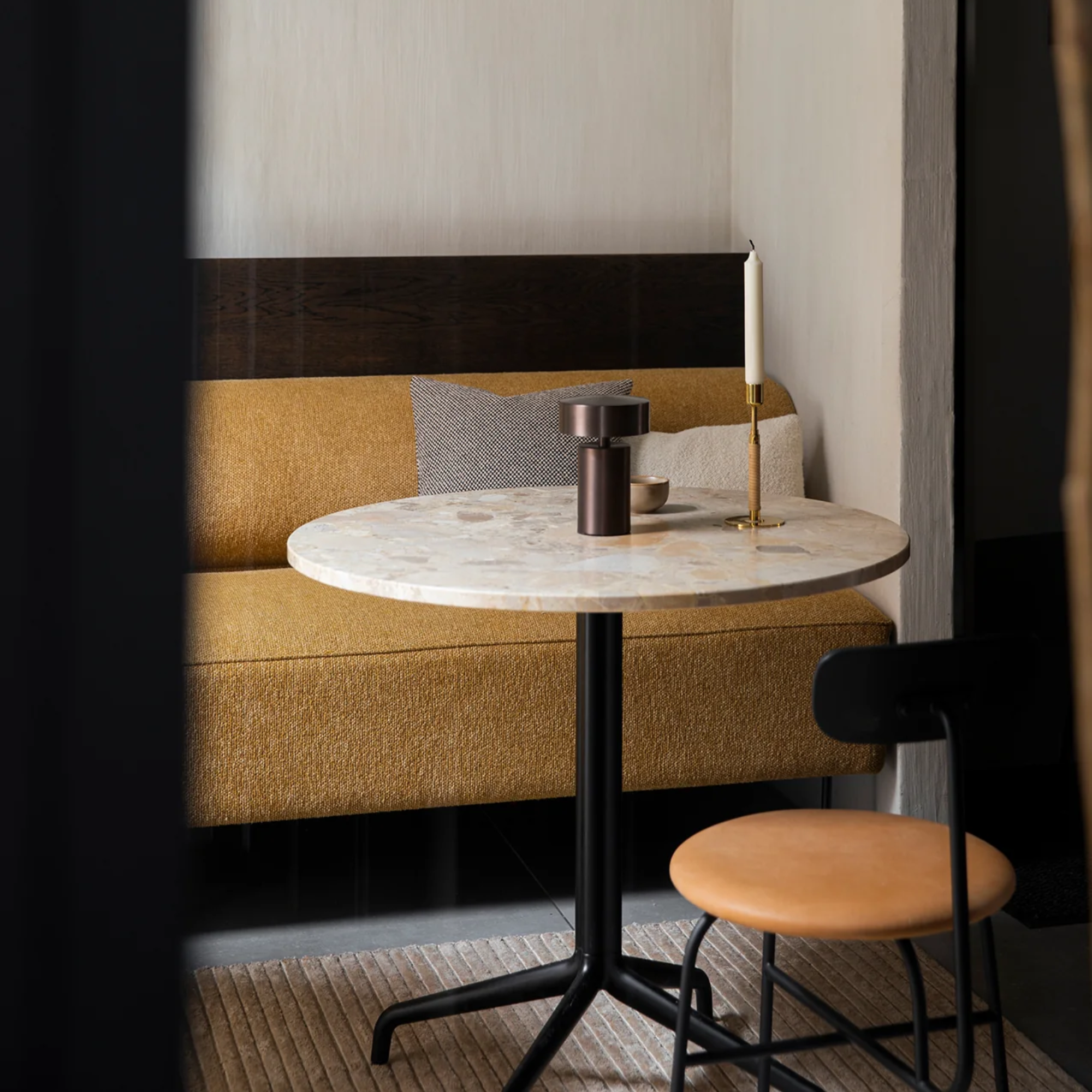 The bronze Column Portable Table Lamp from Audo Copenhagen on a dining table in a small dining area.