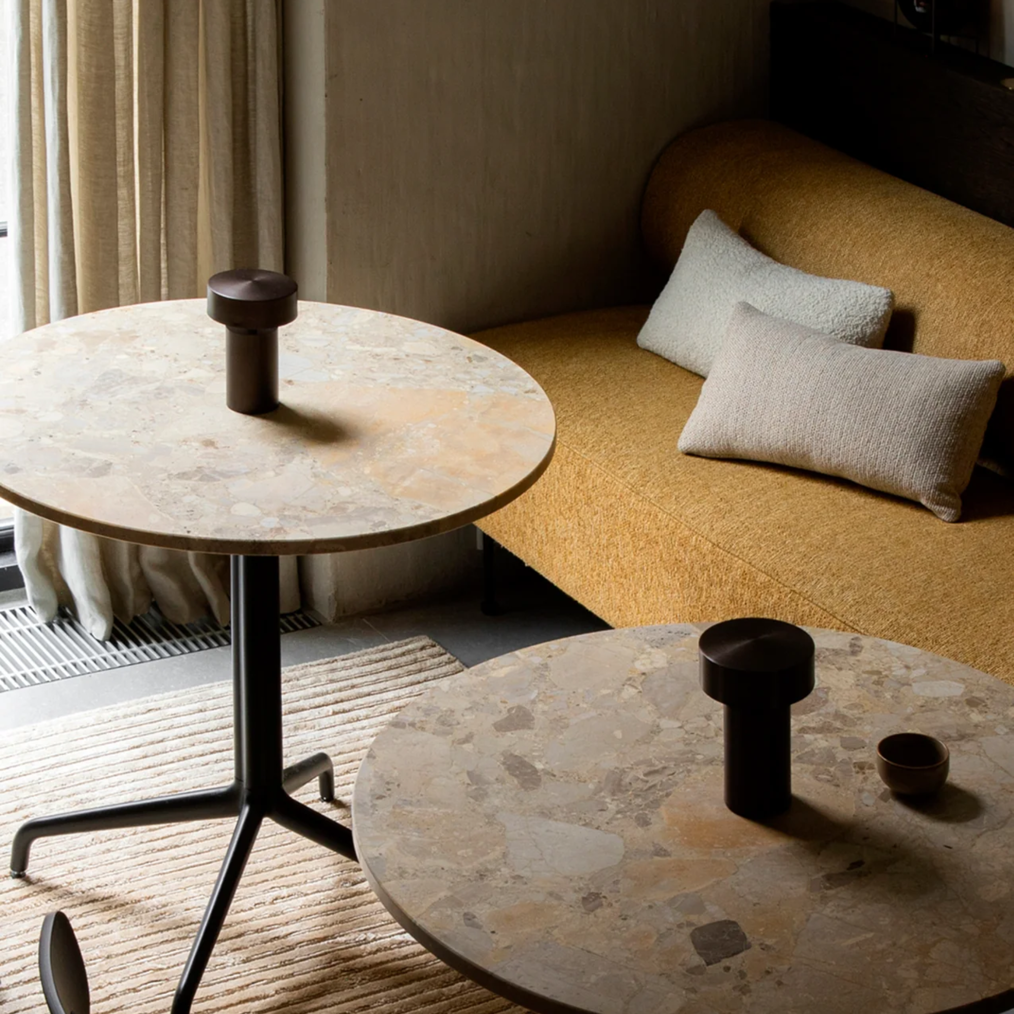 The bronze Column Portable Table Lamp from Audo Copenhagen on a table in a living room near a couch.
