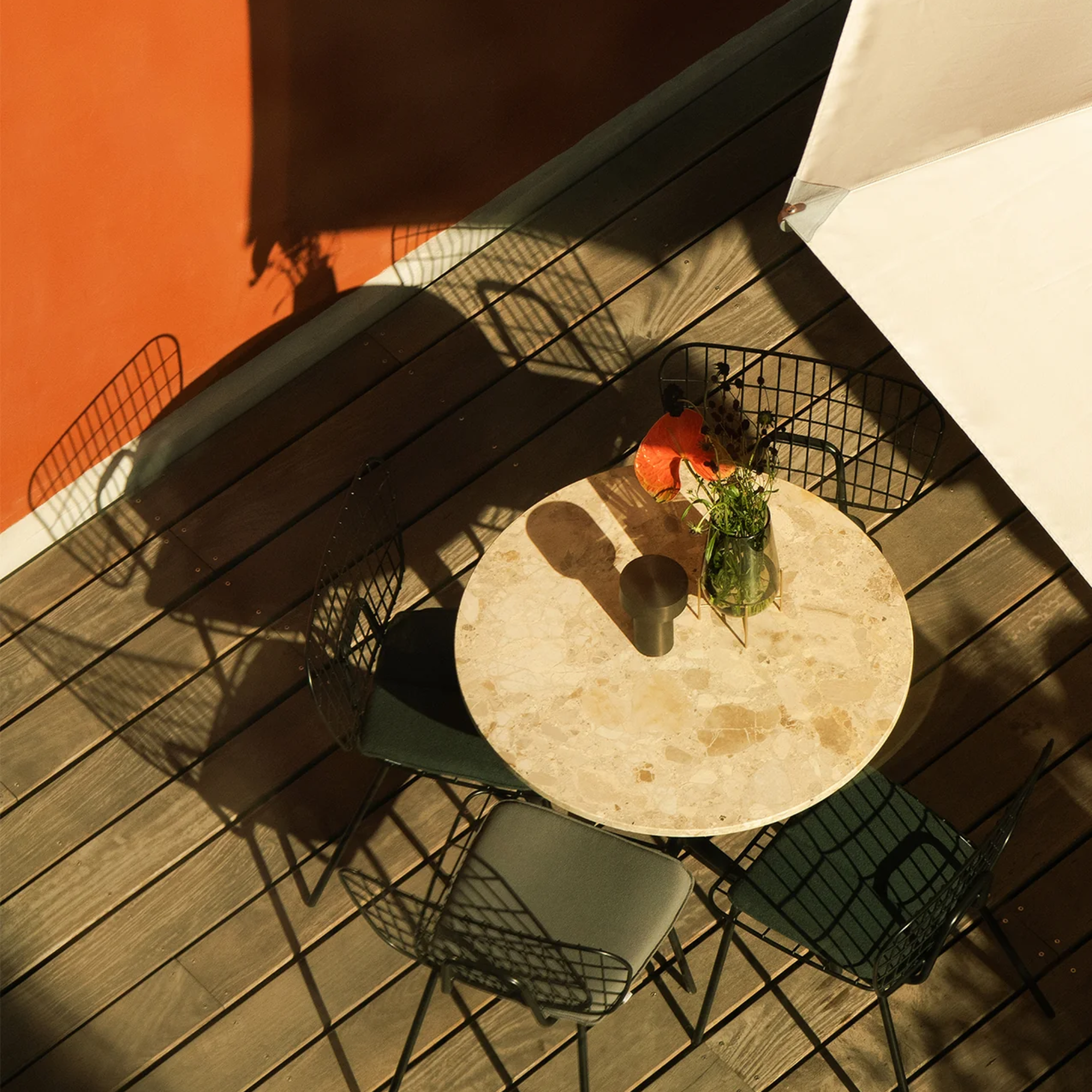 The bronze Column Portable Table Lamp from Audo Copenhagen in an outdoor living area on top of a cafe table surronded by chairs.