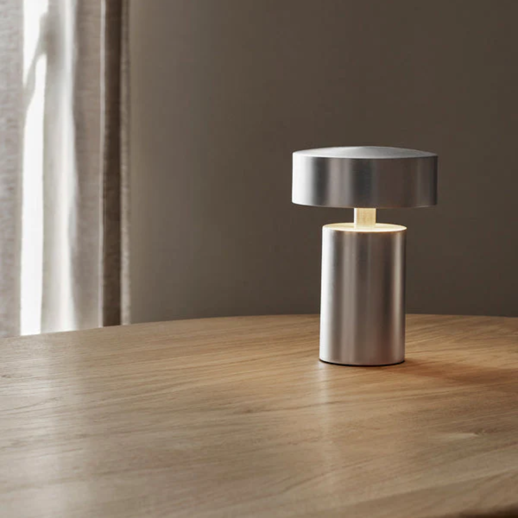 The brushed aluminum Column Portable Table Lamp from Audo Copenhagen in a dining room on top of a wooden dining table.