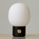 The black JWDA Portable Table Lamp from Audo Copenhagen in a primary bedroom on top of a table.