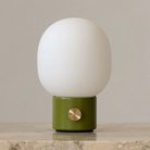 The dusty green JWDA Portable Table Lamp from Audo Copenhagen in a lounge on top of marble furniture.