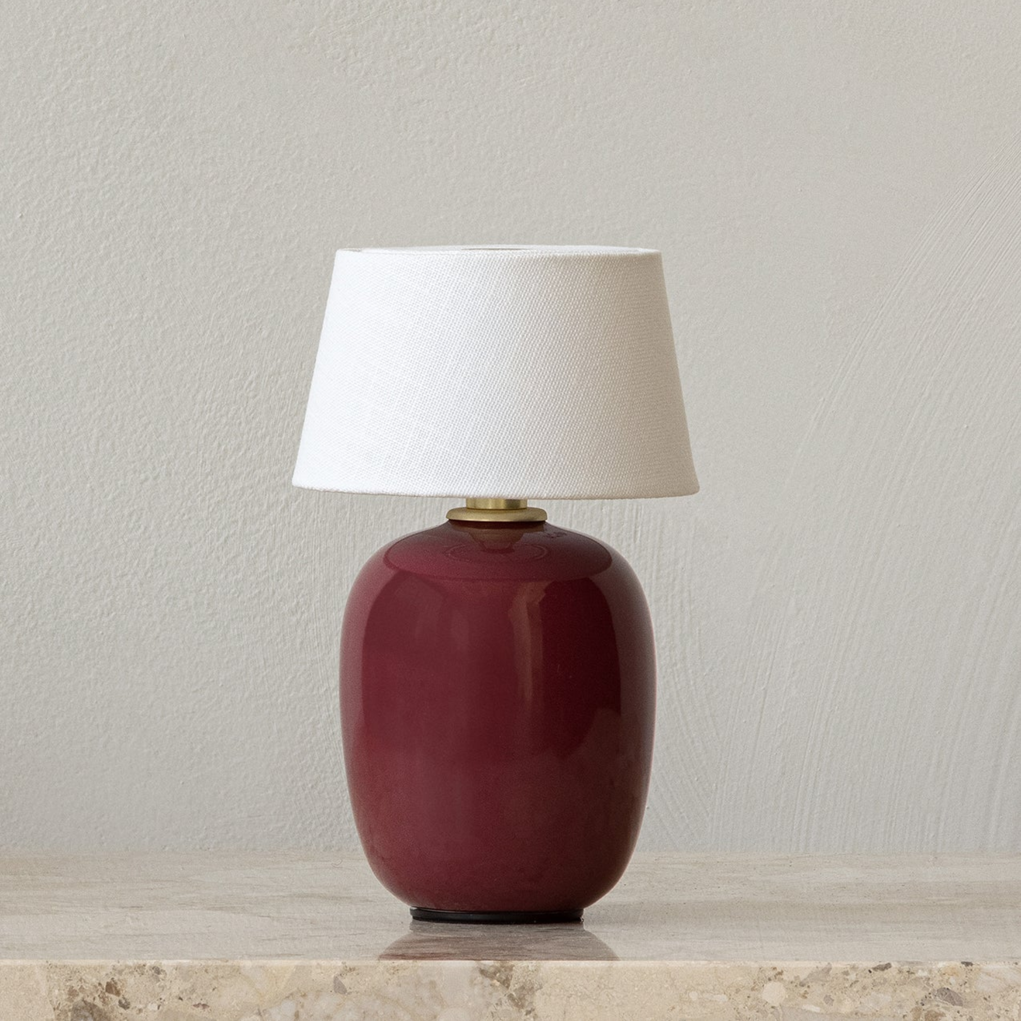 The ruby Torso Portable Table Lamp from Audo Copenhagen in a living room on top of a marble table.