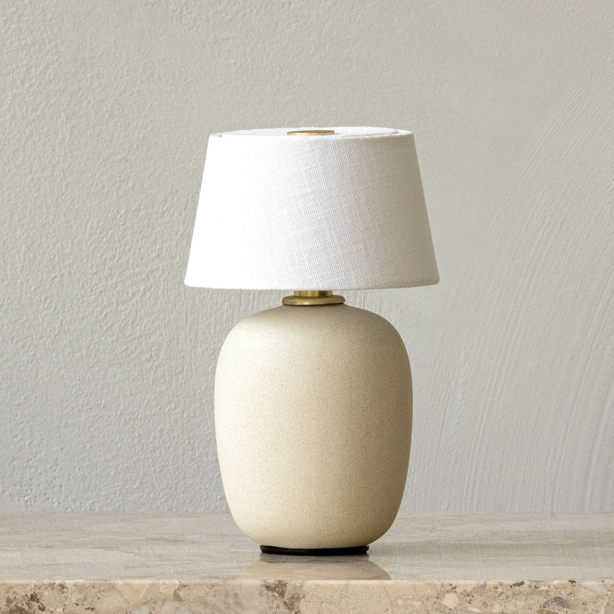 The sand Torso Portable Table Lamp from Audo Copenhagen in a lounge on top of a marble piece of furniture.