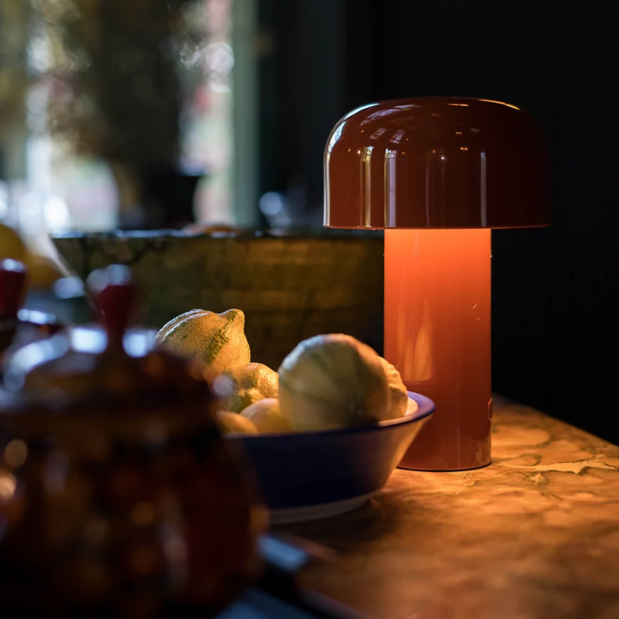 The burnt orange Bellhop Cordless Lamp from FLOS in a kitchen and dining area next to several bowls.