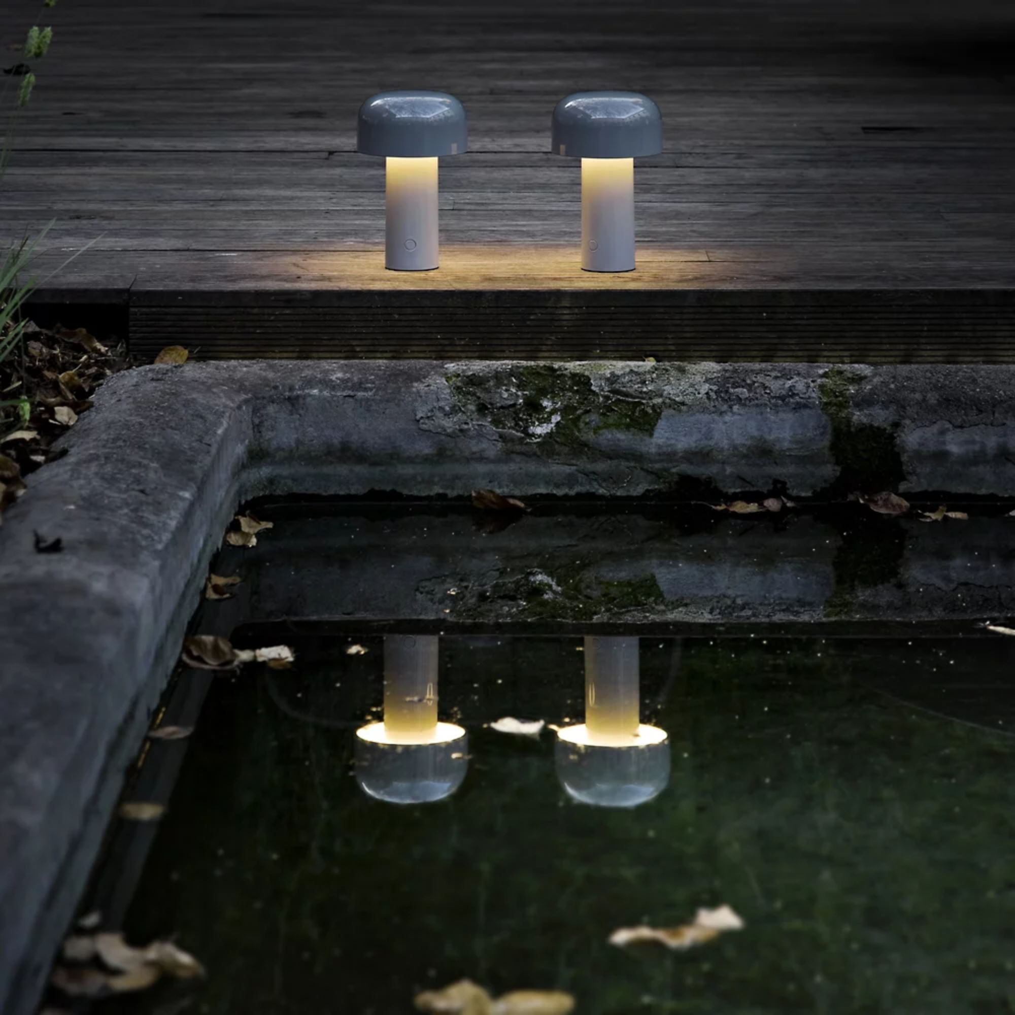 The gray blue Bellhop Cordless Lamp from FLOS next to a pond outdoors.