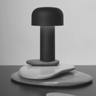 The matte black Bellhop Cordless Lamp from FLOS in a home office on top of stones.