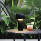 The matte black Bellhop Cordless Lamp from FLOS on top of an outdoor bar table.