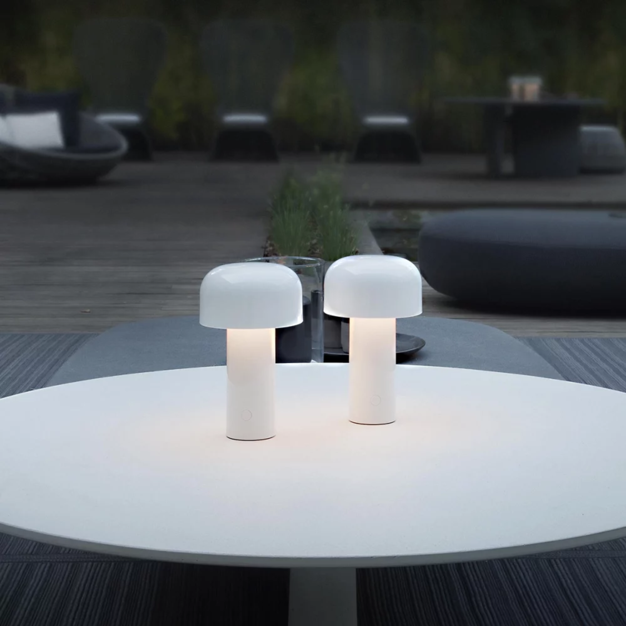 The white Bellhop Cordless Lamp from FLOS in an outdoor living space on top of a coffee table.