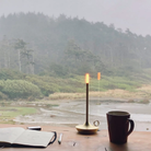 The brass Wick Cordless Lamp from Graypants in a living room overlooking a beach. all-groups