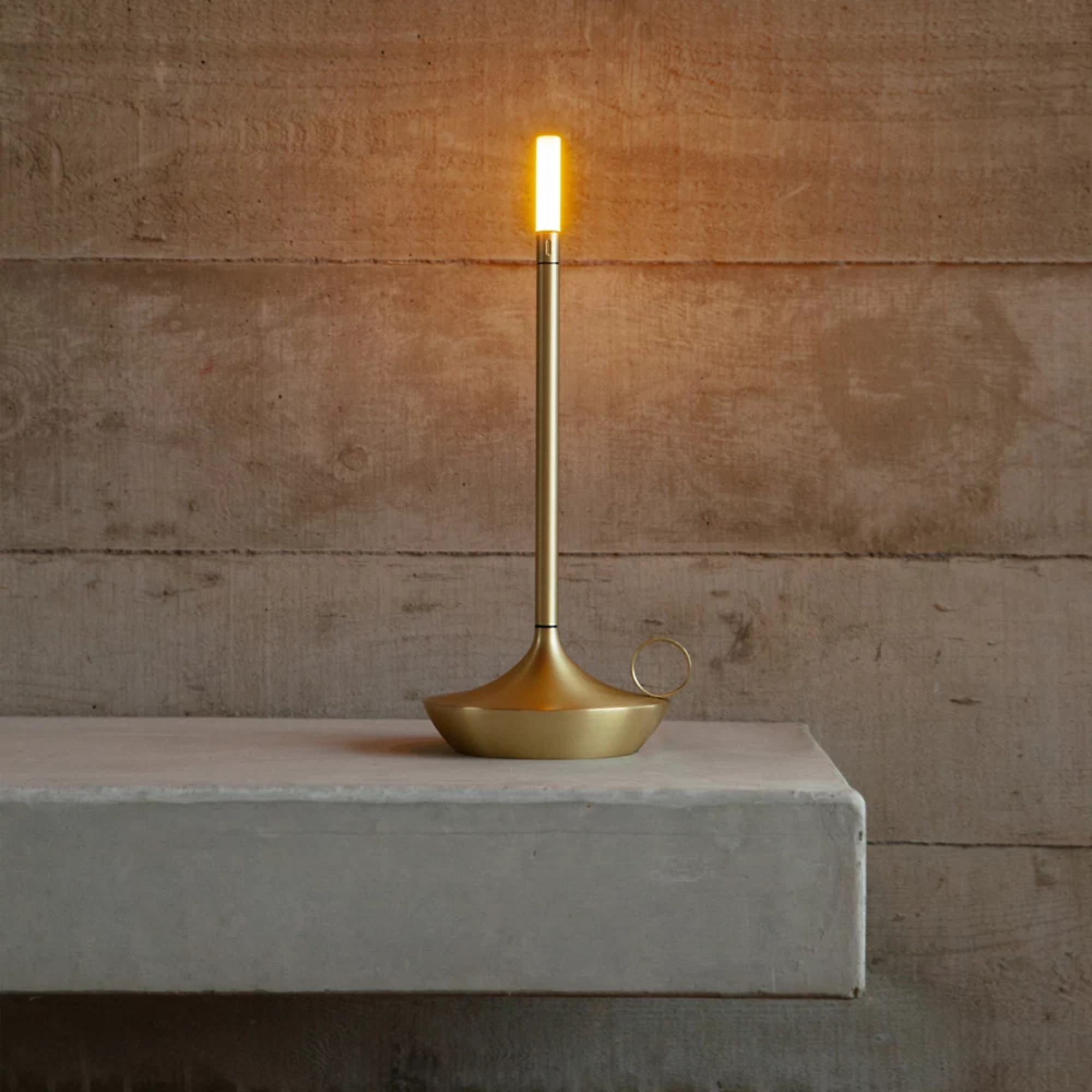 The brass Wick Cordless Lamp from Graypants in a lounge on top of a shelf.