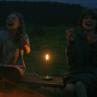 The brass Wick Cordless Lamp from Graypants on a wooden bench between two people eating smores while camping.