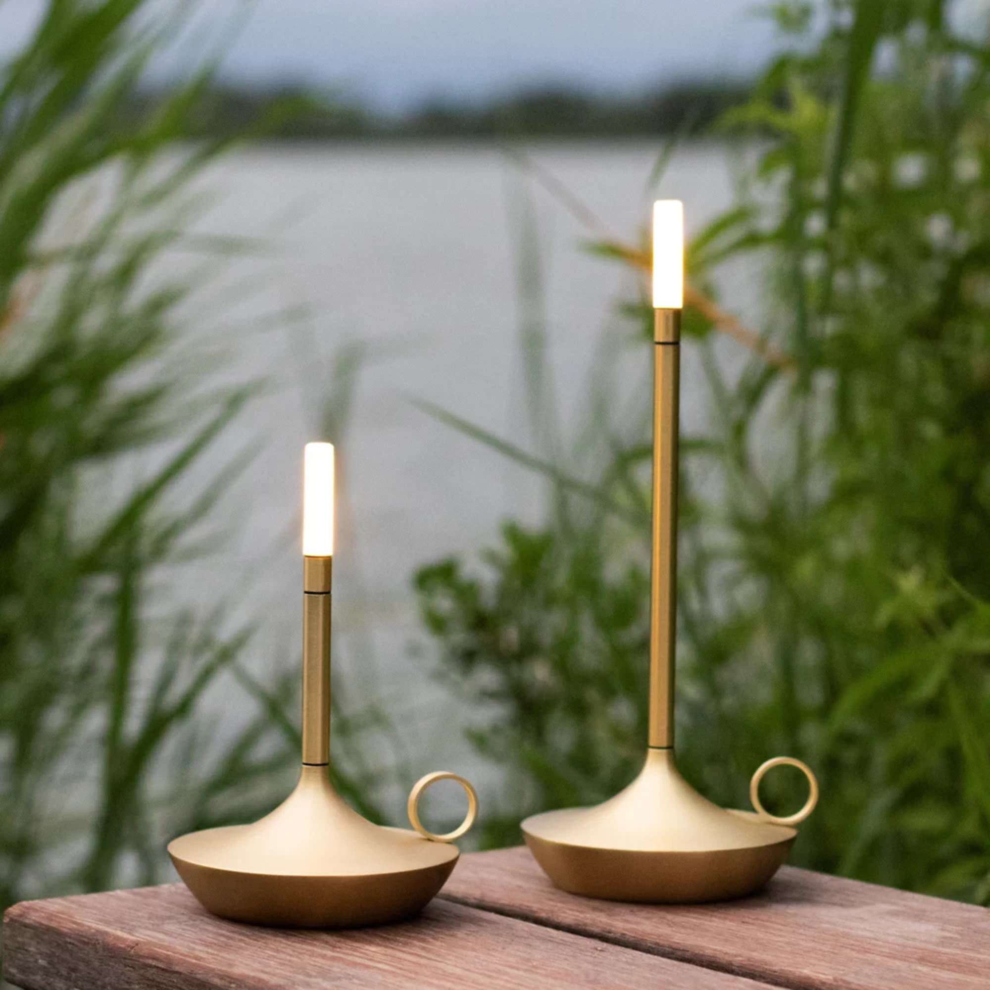 The Wick Pro Cordless Lamp from Graypants in an outdoor living space on top of a wooden surface overlooking a body of water. all-groups