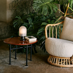 The Seine Portable Table Lamp from GUBI in an outdoor terrace on a side table next to a lounge chair and monstera.