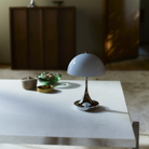 The grey opal Panthella 160 Portable Lamp from Louis Poulsen in a home library on top of a coffee table for books and reading.