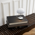 The grey opal Panthella 160 Portable Lamp from Louis Poulsen in a home office on top of a stack of books on a bench.