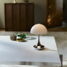 The grey opal Panthella 160 Portable Lamp from Louis Poulsen in a tv room on top of a table.