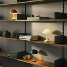 The opal beige Panthella 160 Portable Lamp from Louis Poulsen in a home office on a shelving unit with other lights.