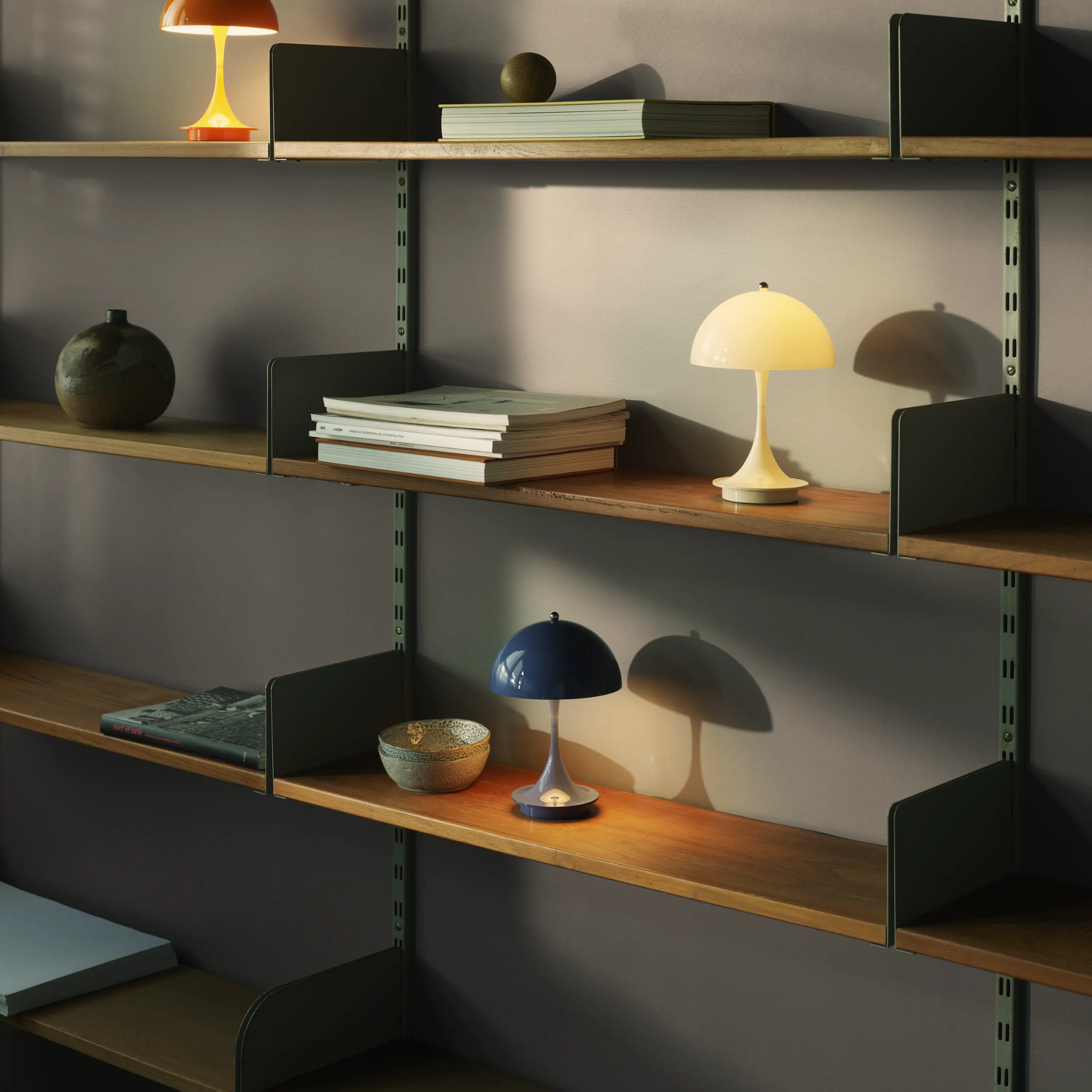 The opaque indigo Panthella 160 Portable Lamp from Louis Poulsen in a home office on a shelf with bowls and other decor.