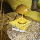 The opaque yellow Panthella 160 Portable Lamp from Louis Poulsen in a living room on top of a side table with books.