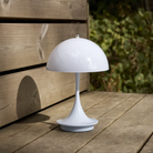 The pale blue opal Panthella 160 Portable Lamp from Louis Poulsen in a garden on top of a wooden bench.