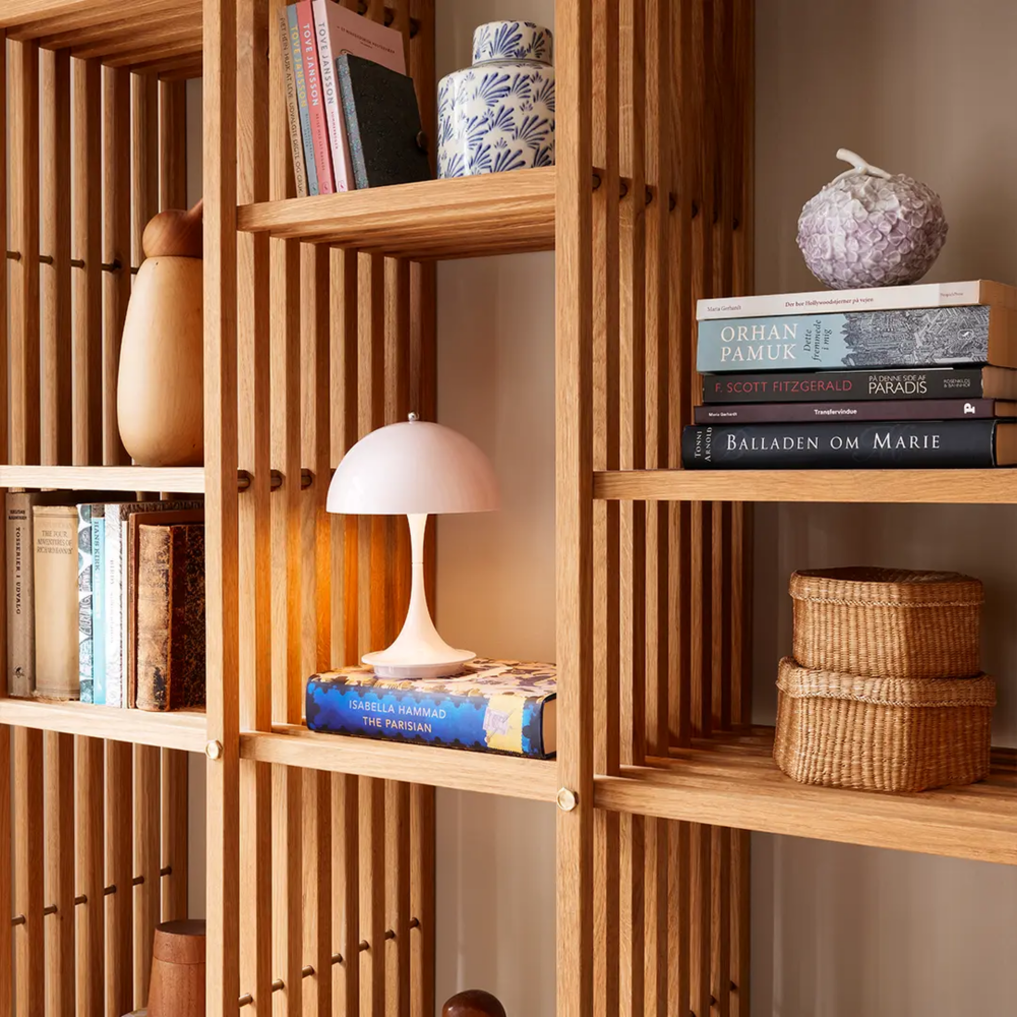 The pale rose opal Panthella 160 Portable Lamp from Louis Poulsen in a home office with other decor on a bookshelf.