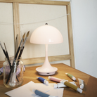 The pale rose opal Panthella 160 Portable Lamp from Louis Poulsen in a lounge with art supplies.