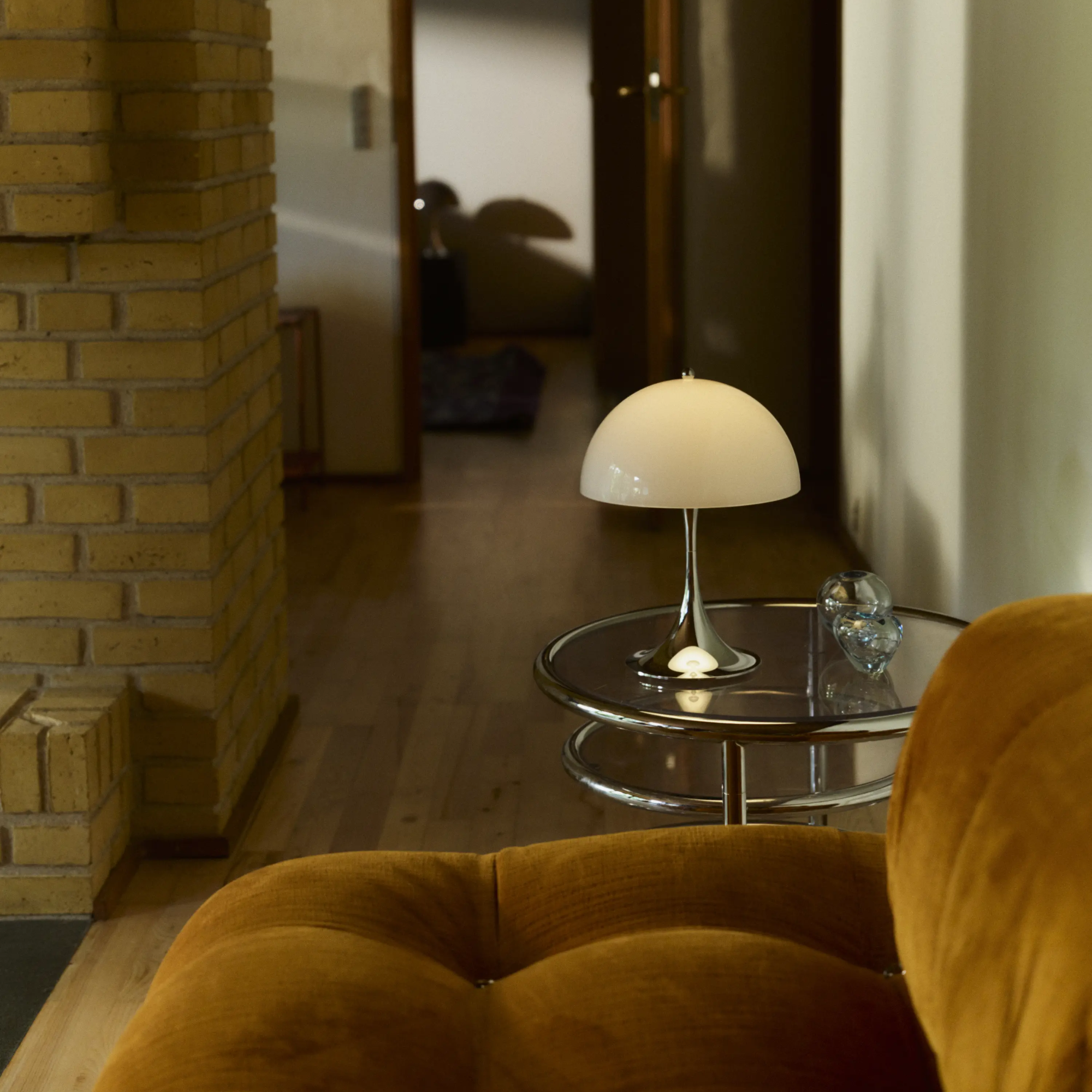 The grey opal Panthella 250 Portable Lamp from Louis Poulsen in a living space on top of a table beside a couch.