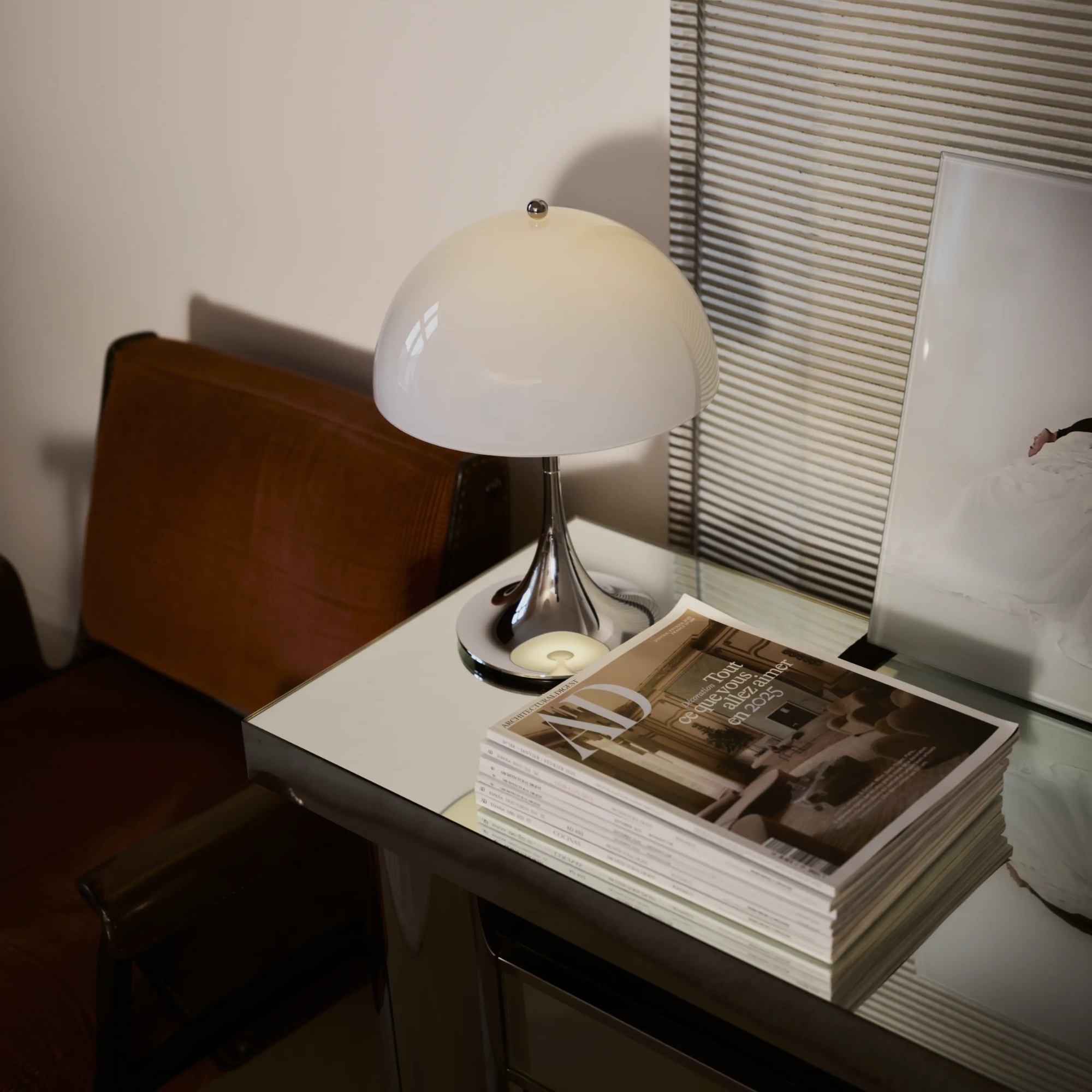 The grey opal Panthella 250 Portable Lamp from Louis Poulsen in a lounge on top of a desk beside a chair.