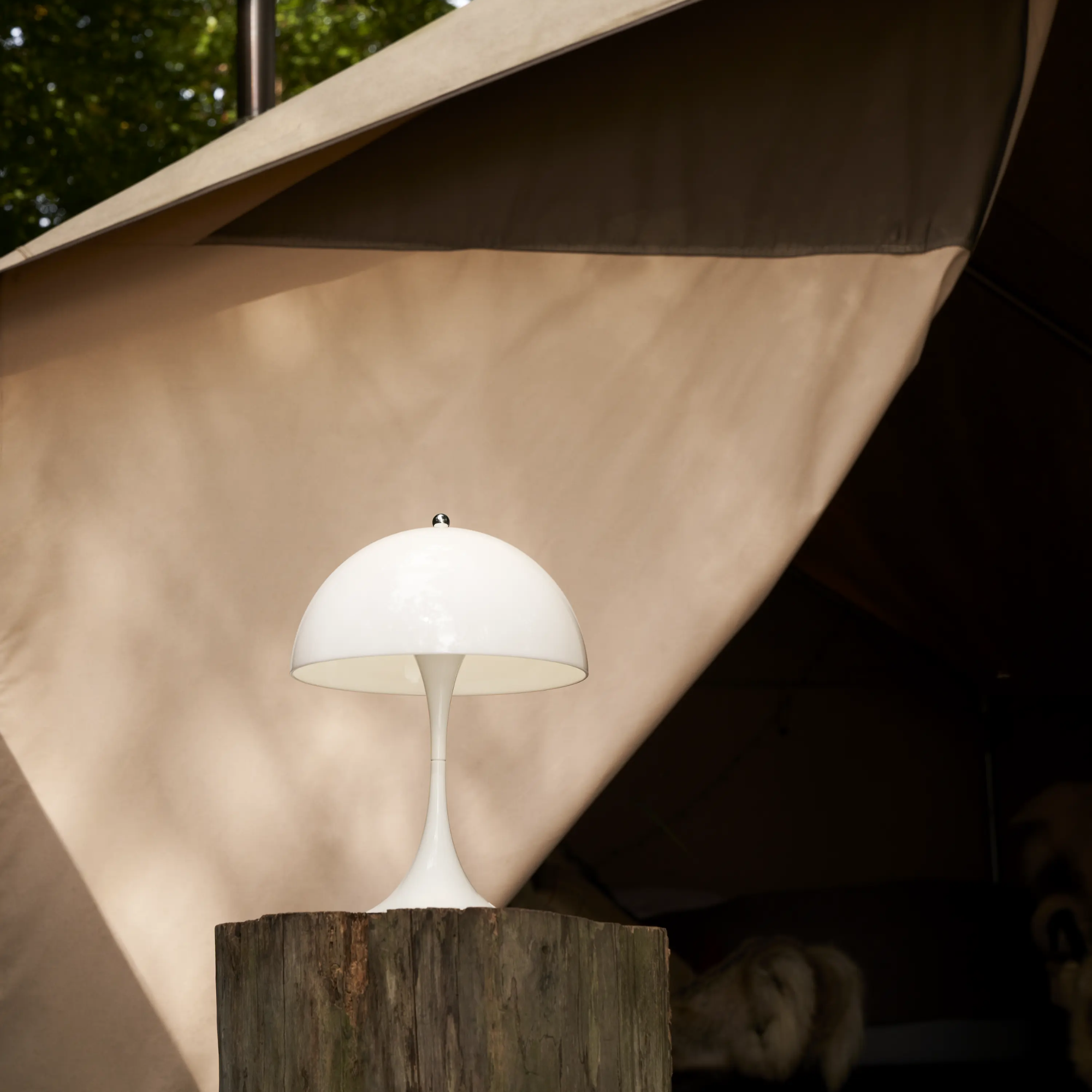 The opal Panthella 250 Portable Lamp from Louis Poulsen used on a log of wood in an outdoor terrace.